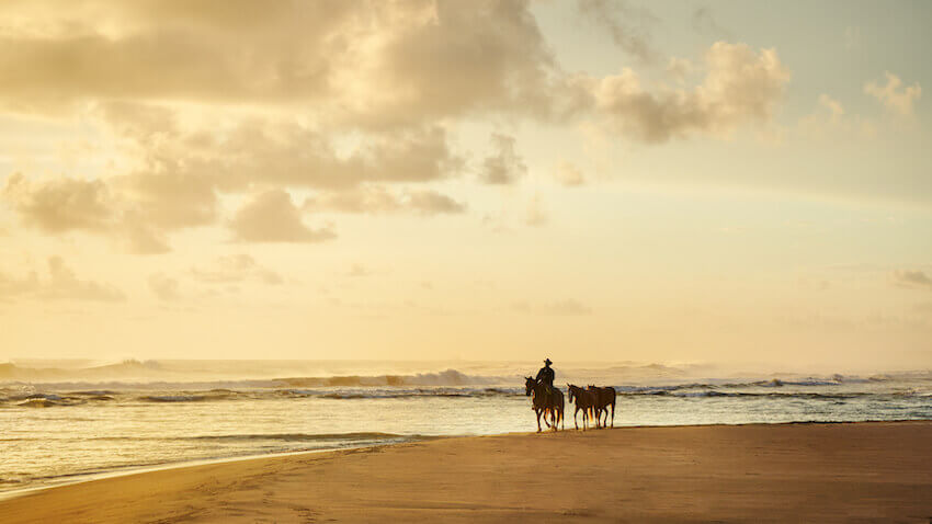 Men riding a horse on the beach.